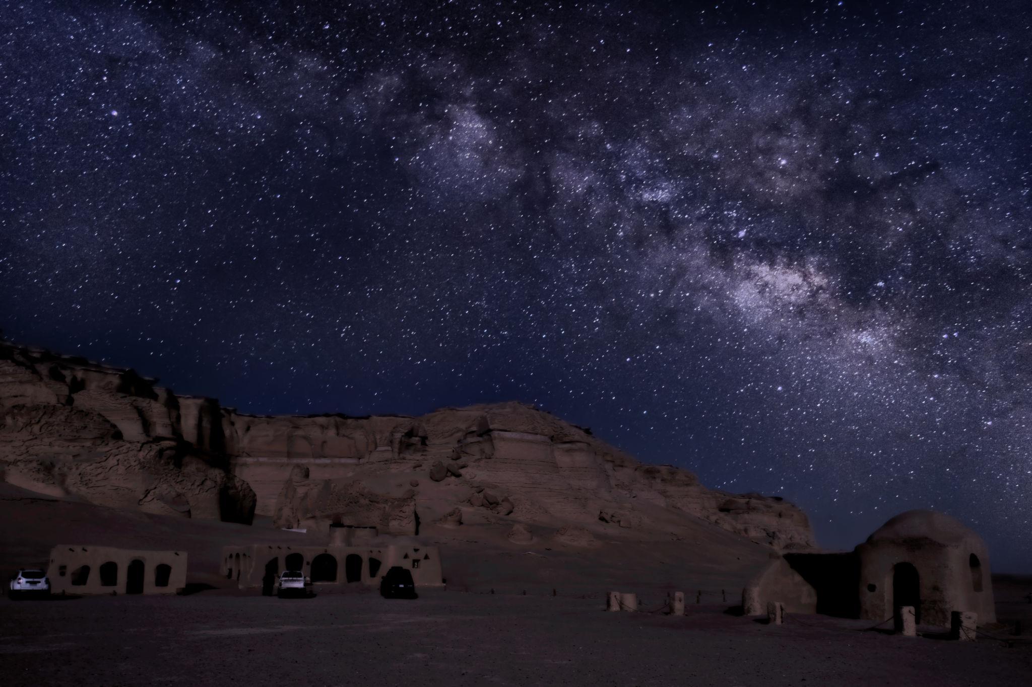 The Milky Way arching over ancient desert cliffs and cave dwellings in Fayoum at night