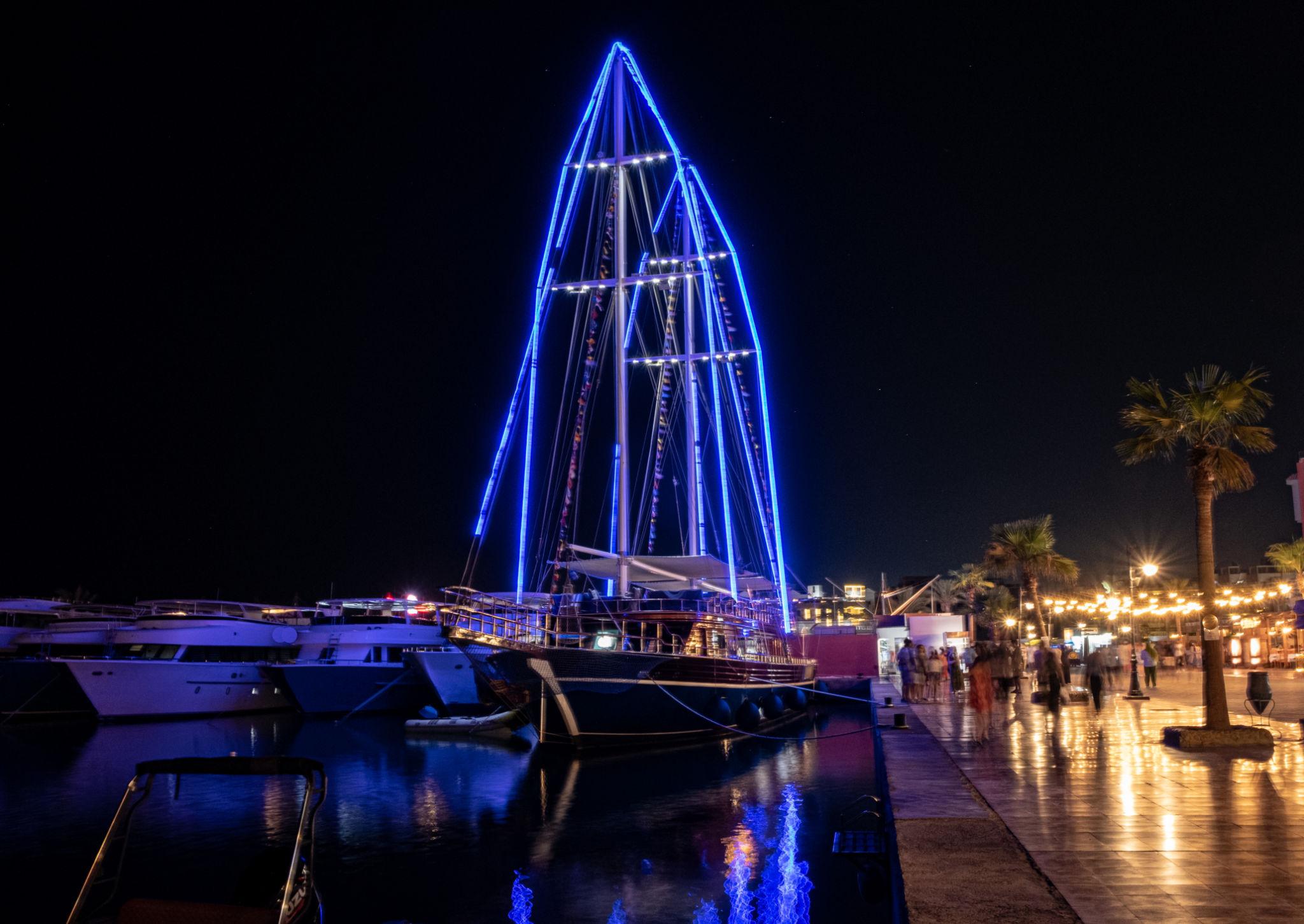 A tall sailboat outlined in blue neon lights moored at a Red Sea marina at night