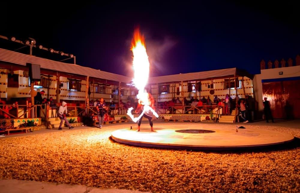 Fire performer spinning flames on a circular stage at a Red Sea desert camp at night