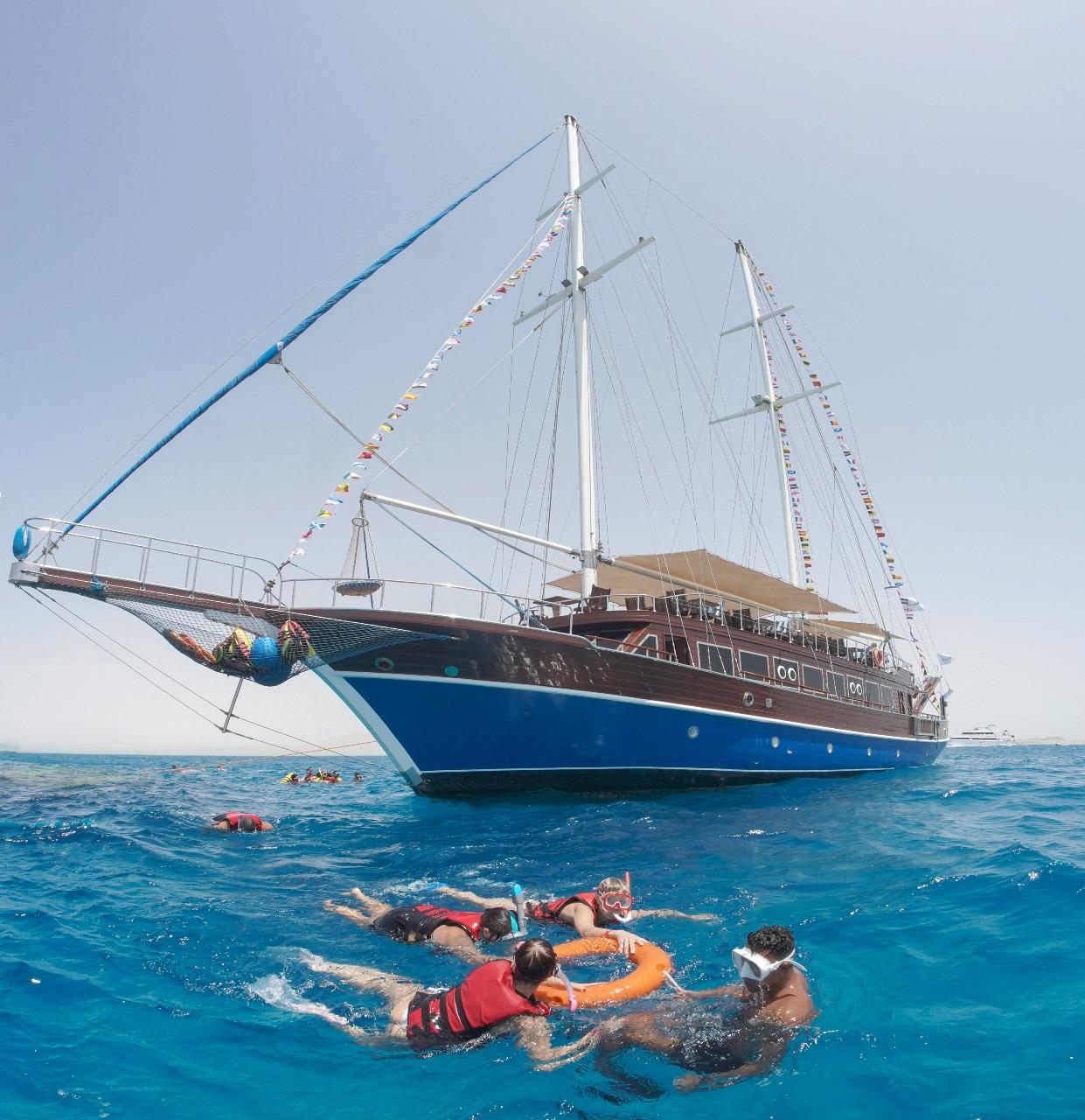 Group of snorkelers in life jackets swimming beside a large wooden gulet in the Red Sea