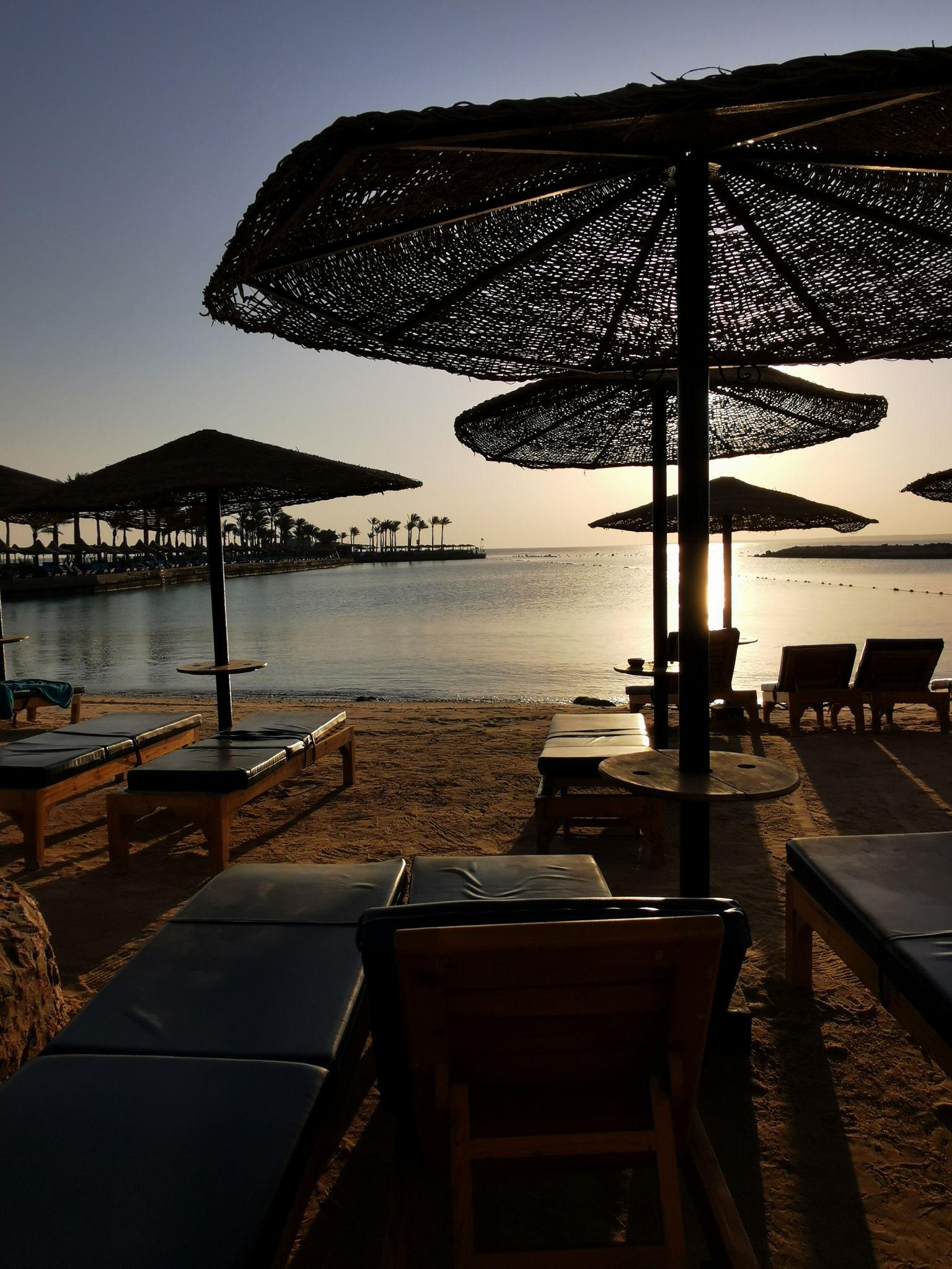 Silhouetted thatched beach umbrellas and sun loungers at sunset on the Red Sea shore