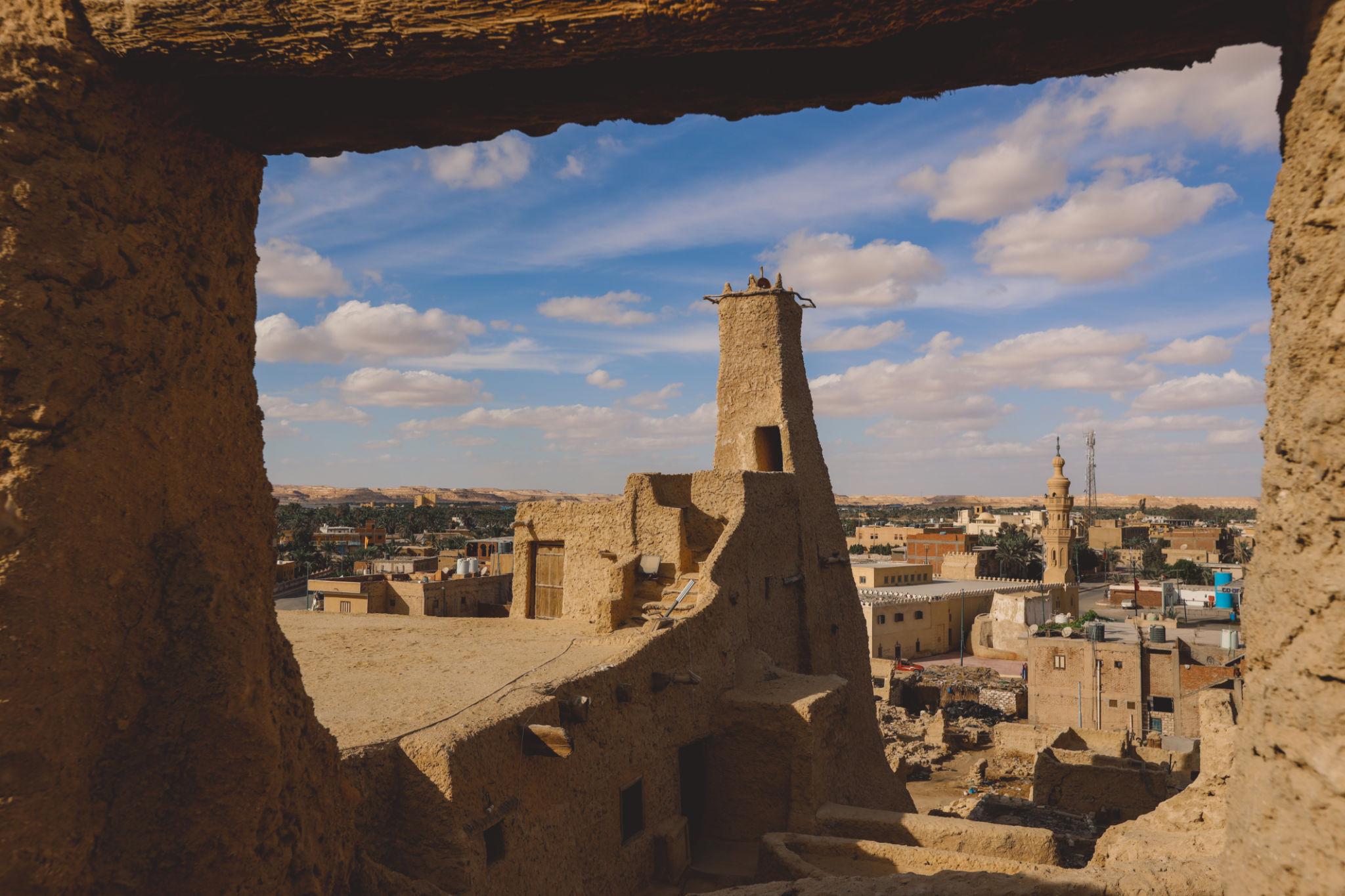 Ancient mud-brick minaret and rooftops of Siwa Oasis framed through a stone window opening