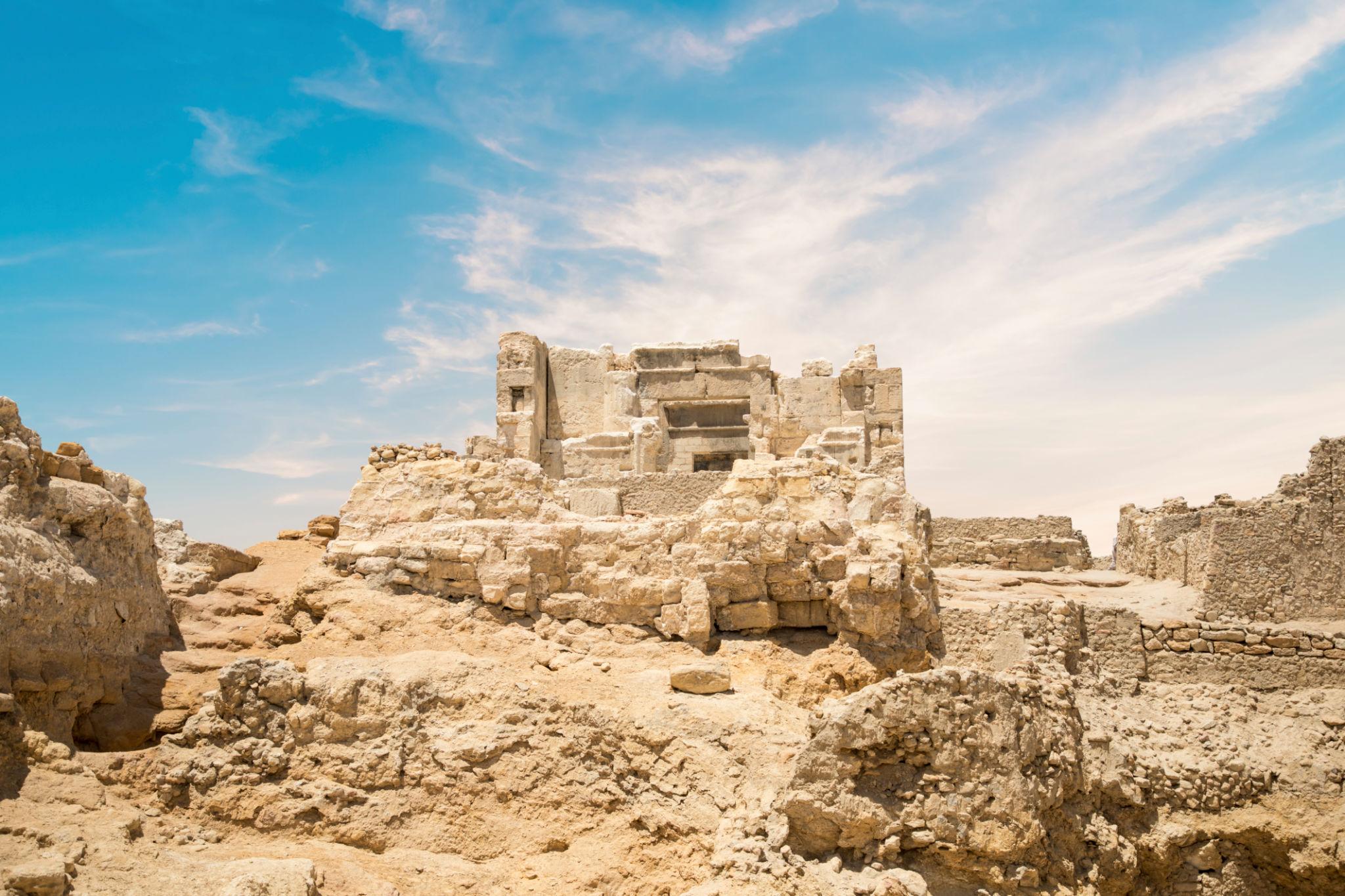 Ancient crumbling stone ruins of the Oracle Temple at Siwa Oasis under a blue sky