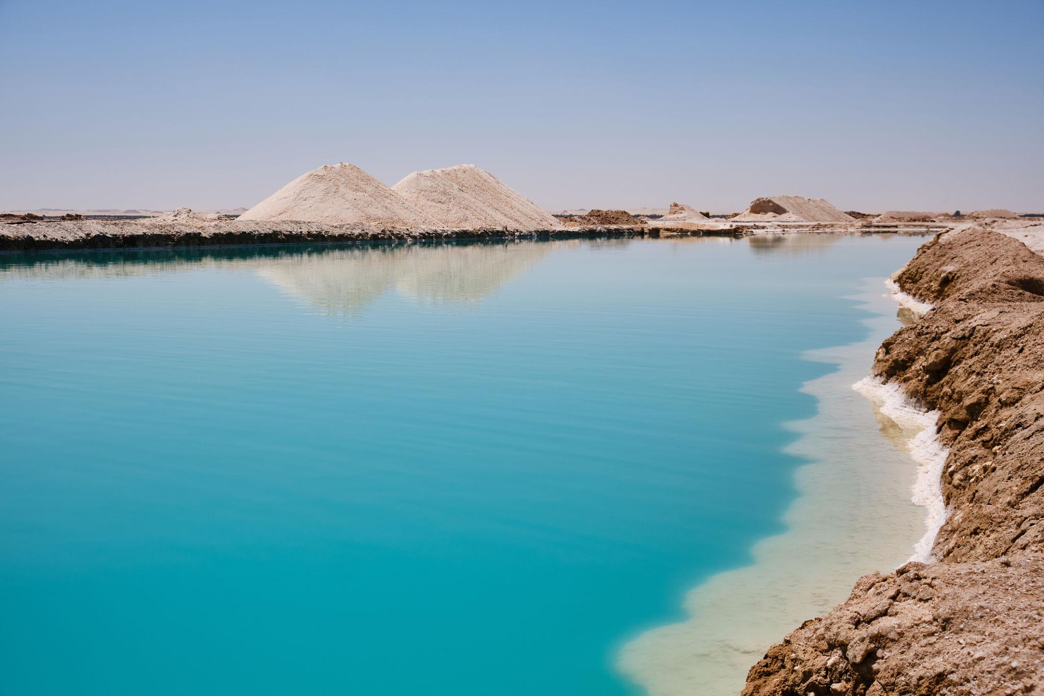 Vivid turquoise salt lake with white salt mounds reflected on the still water in Siwa.