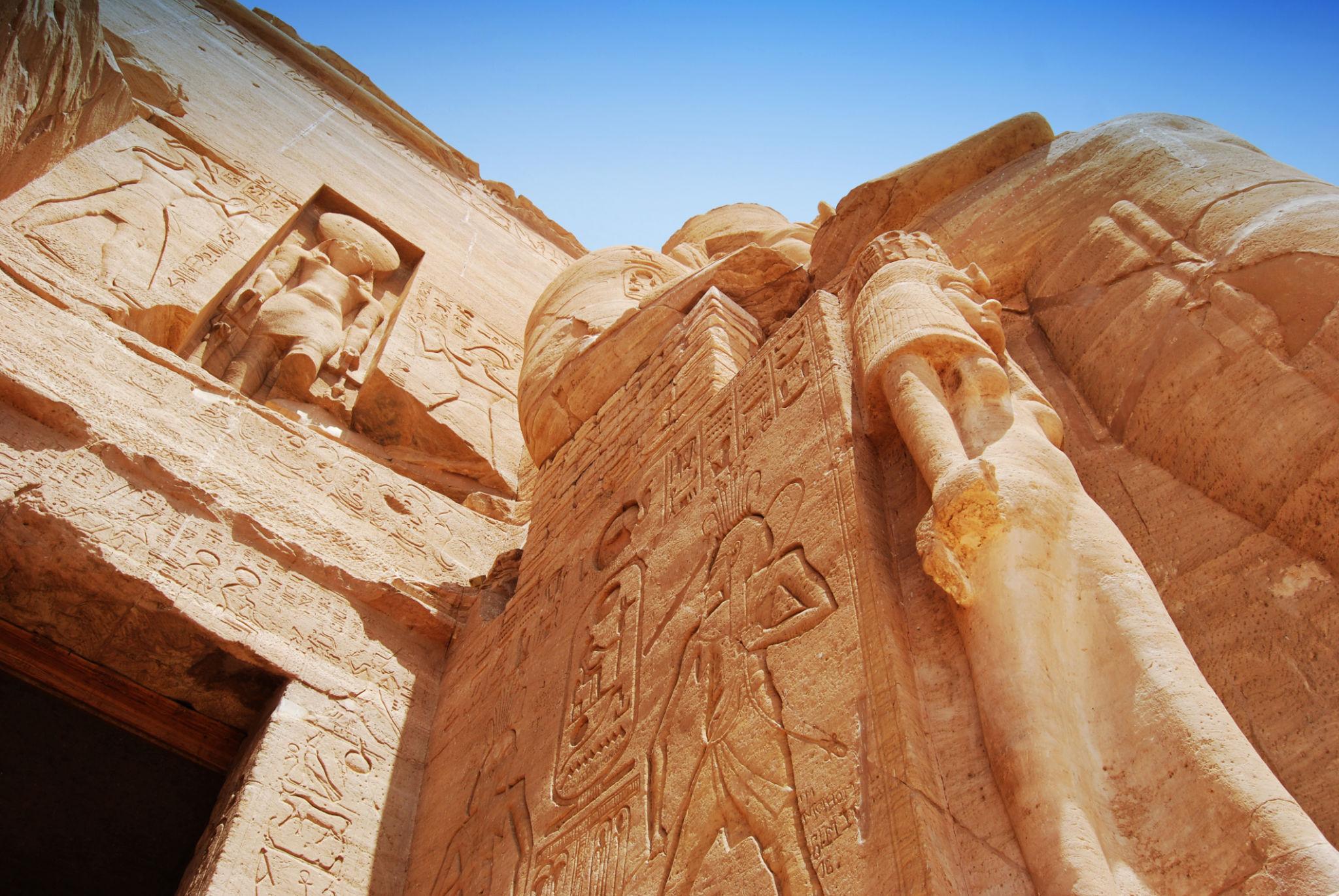 Low-angle view of Abu Simbel's carved sandstone facade with hieroglyphs and colossal figures.