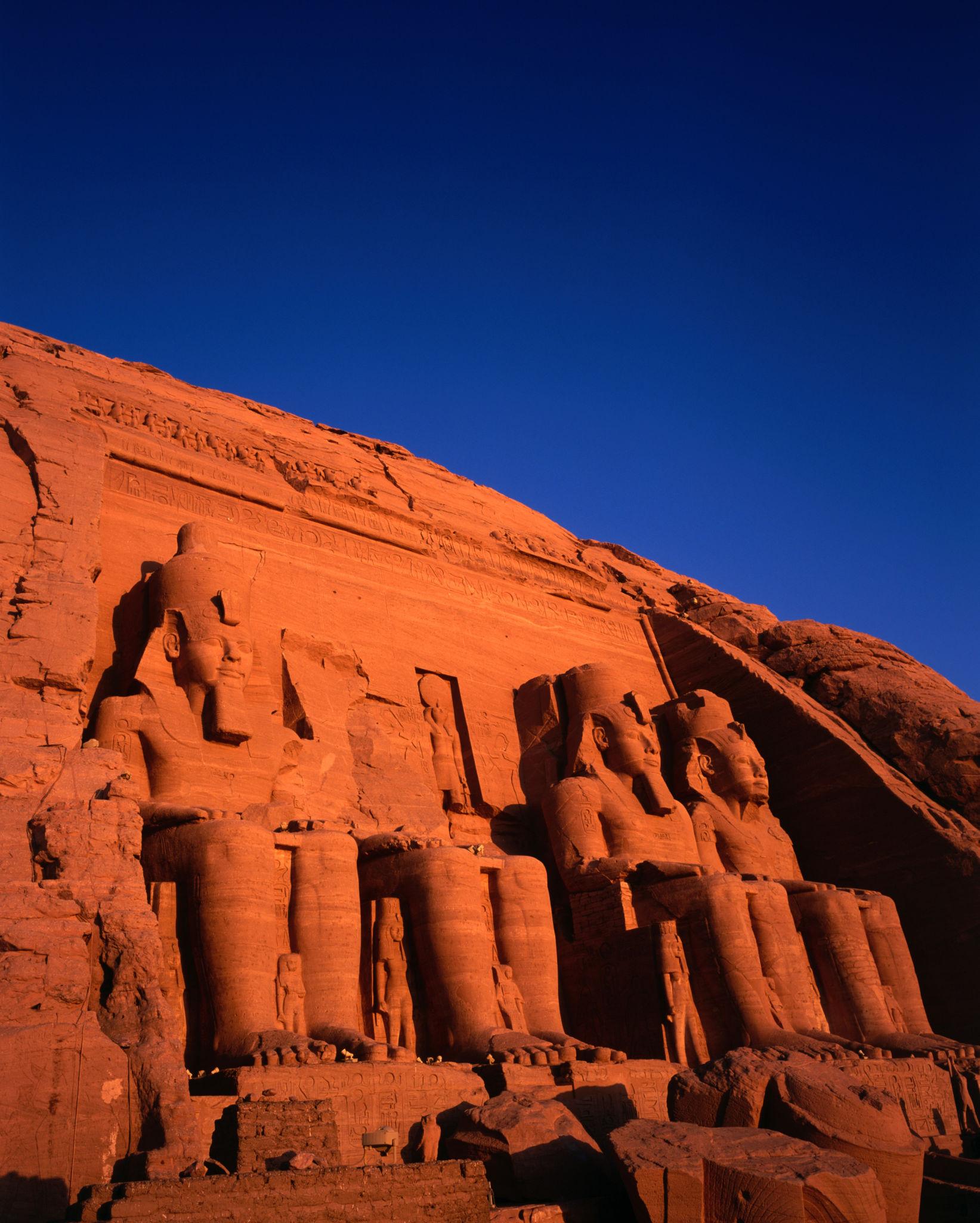 Colossal seated statues of Ramesses II carved into the cliff facade of the Great Temple at Abu Simbel glowing in warm sunset light