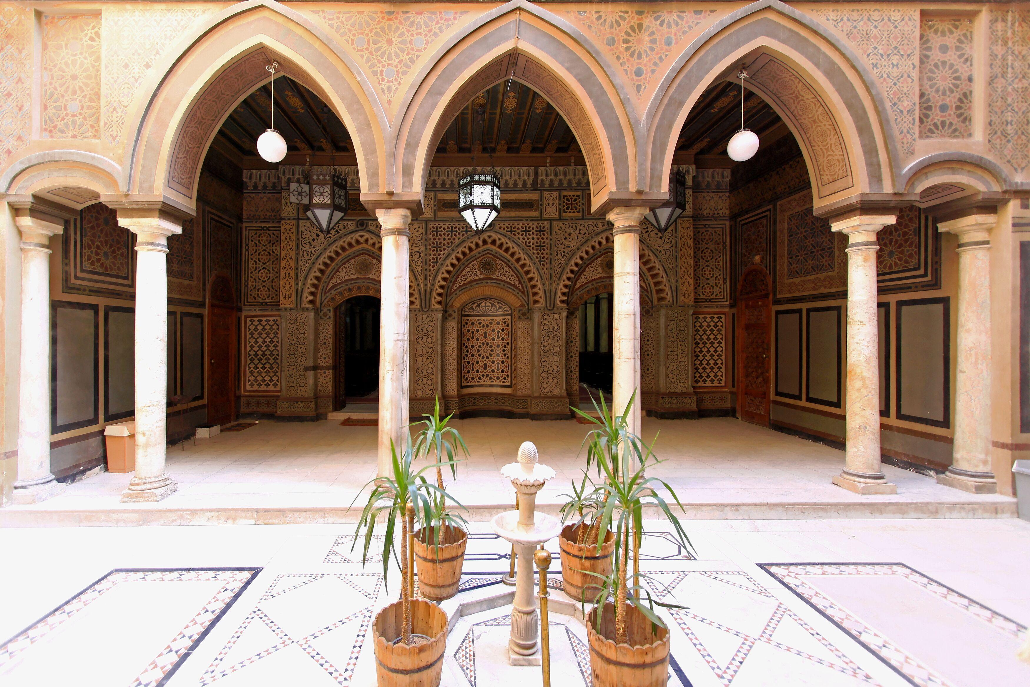 Ornate Mamluk-style courtyard with pointed arches, marble columns, and a central fountain