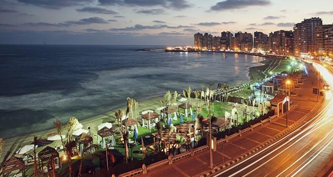 Alexandria Corniche at twilight with illuminated seafront road, beach umbrellas and Mediterranean bay curve