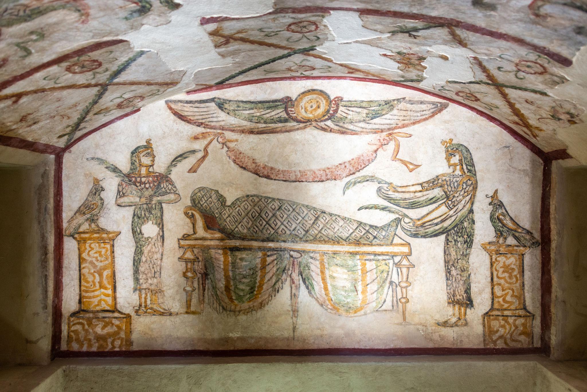 Colorful painted fresco showing Anubis preparing a mummy beneath a winged sun disk
