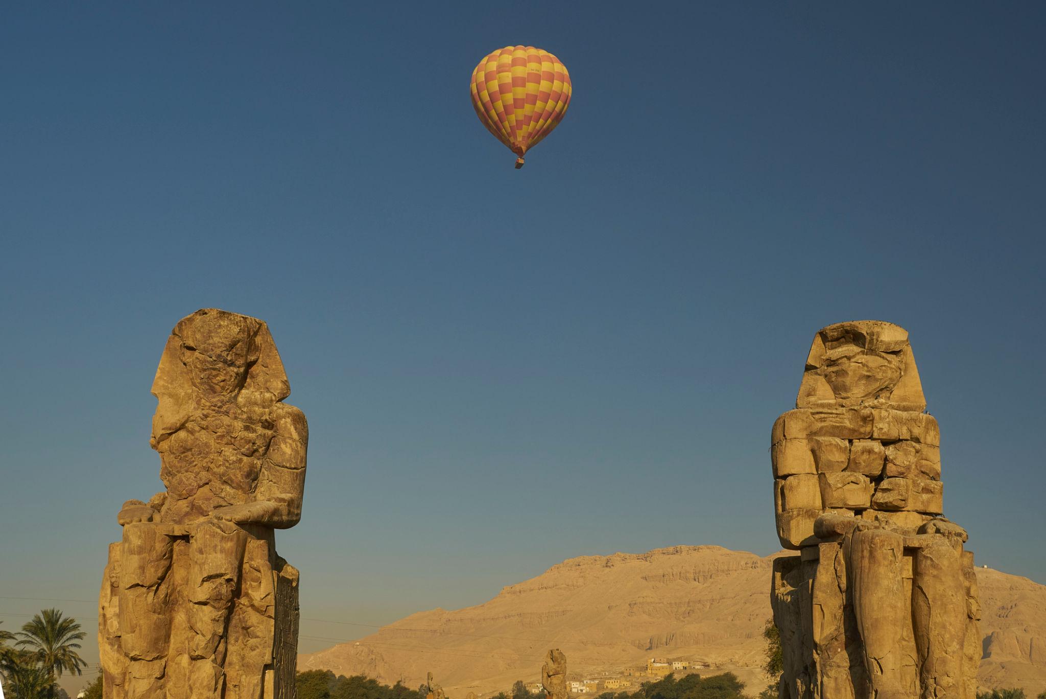 Hot air balloon drifts between the Colossi of Memnon at sunrise over Luxor