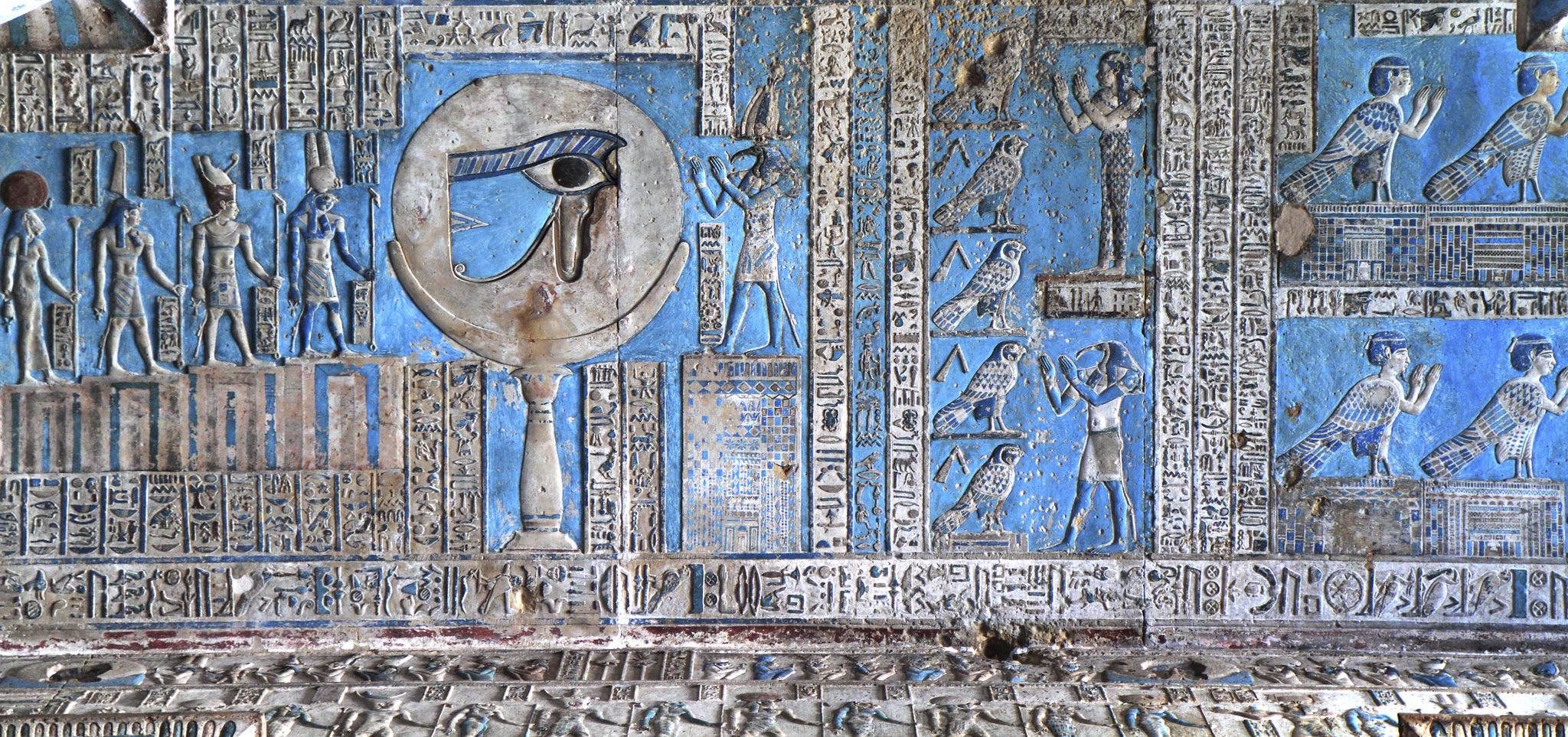 Large Eye of Horus wedjat relief on a blue-painted wall with offering scenes.