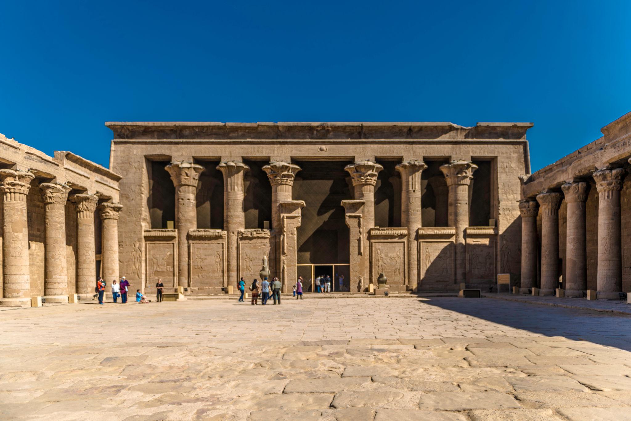 Interior facade of the colonnaded forecourt at the Temple of Edfu under blue sky.