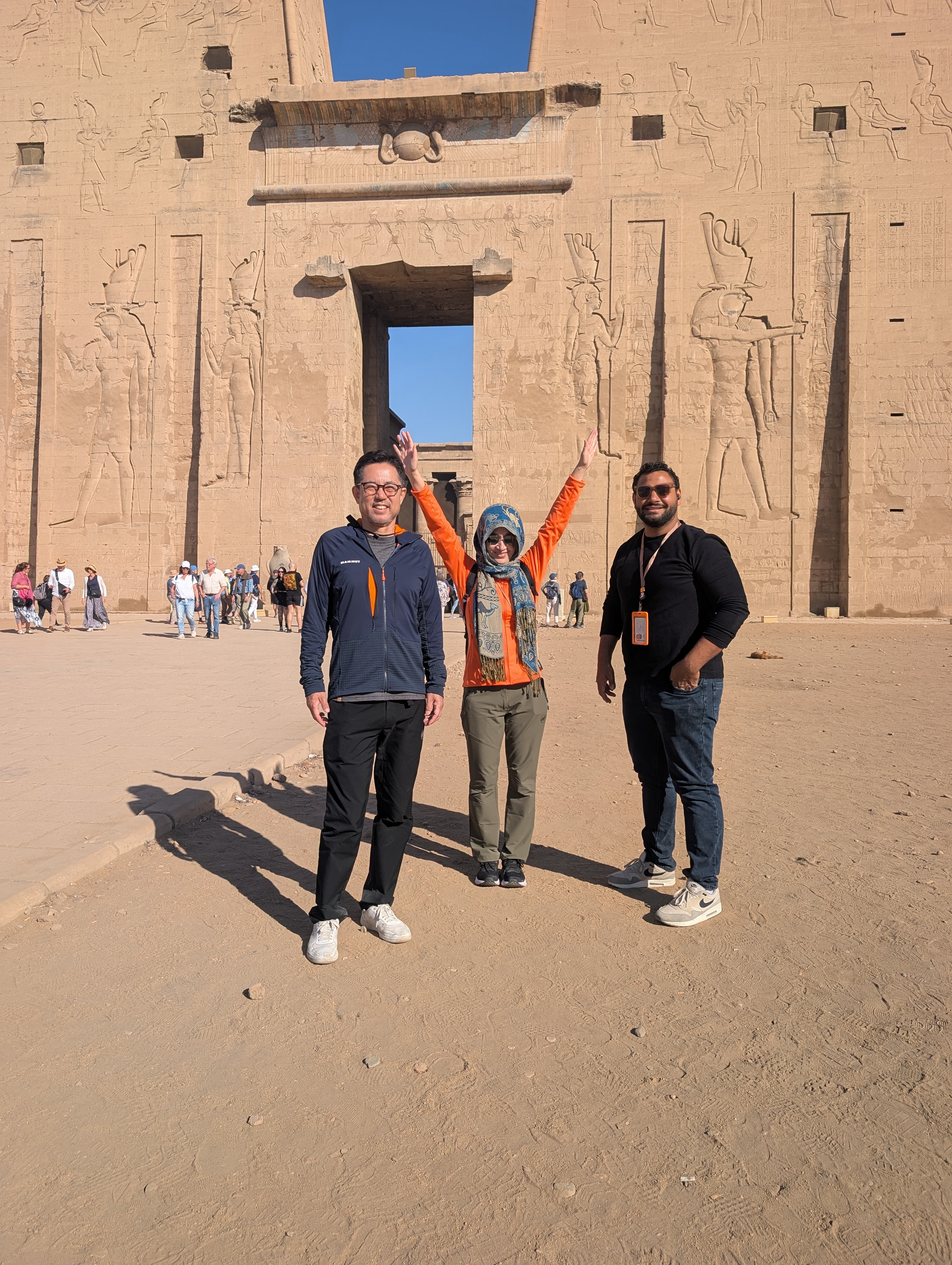 Three travellers posing joyfully in front of the gateway at the Temple of Edfu.
