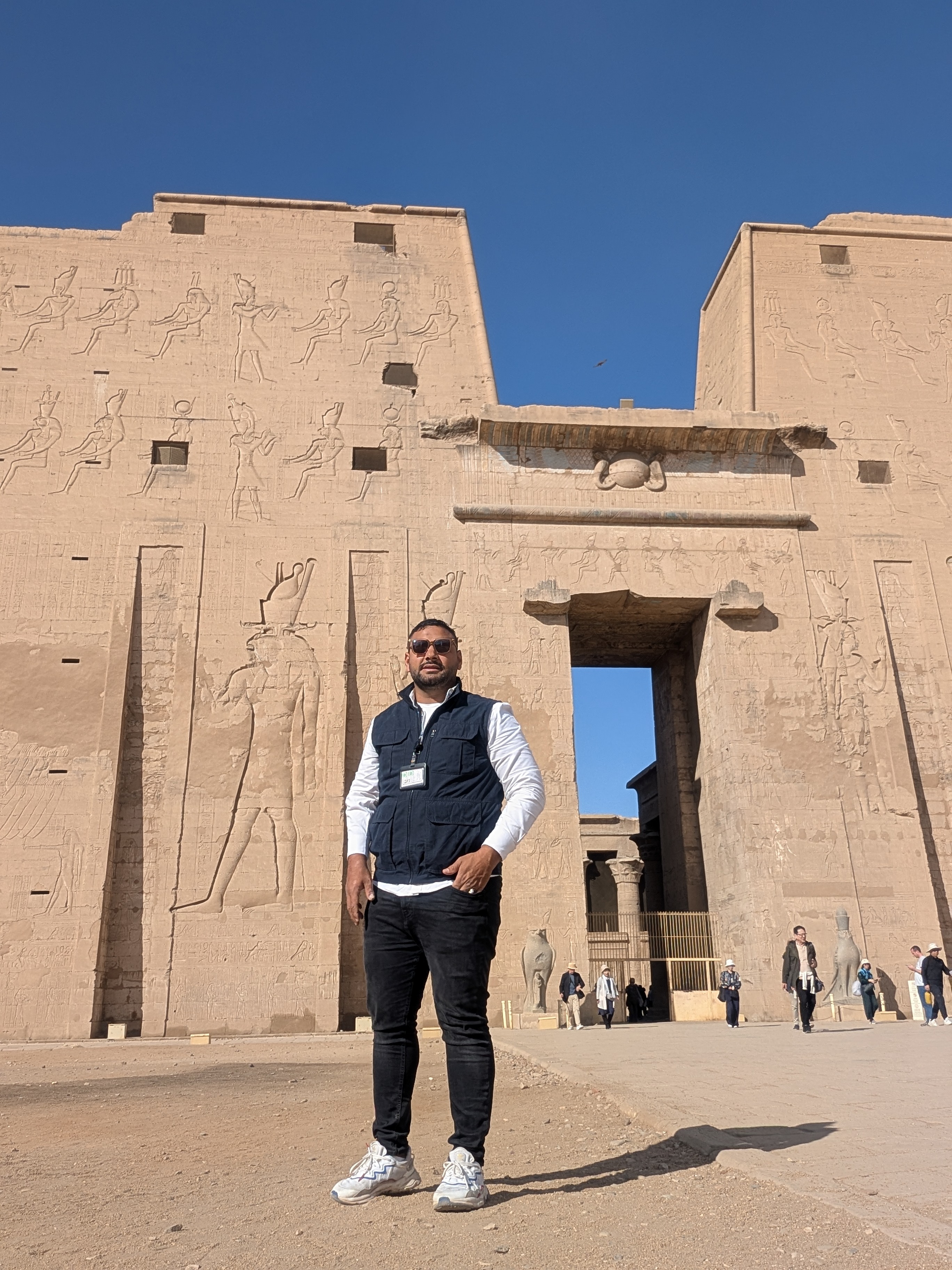 Tour guide standing in front of the towering Temple of Edfu pylon.