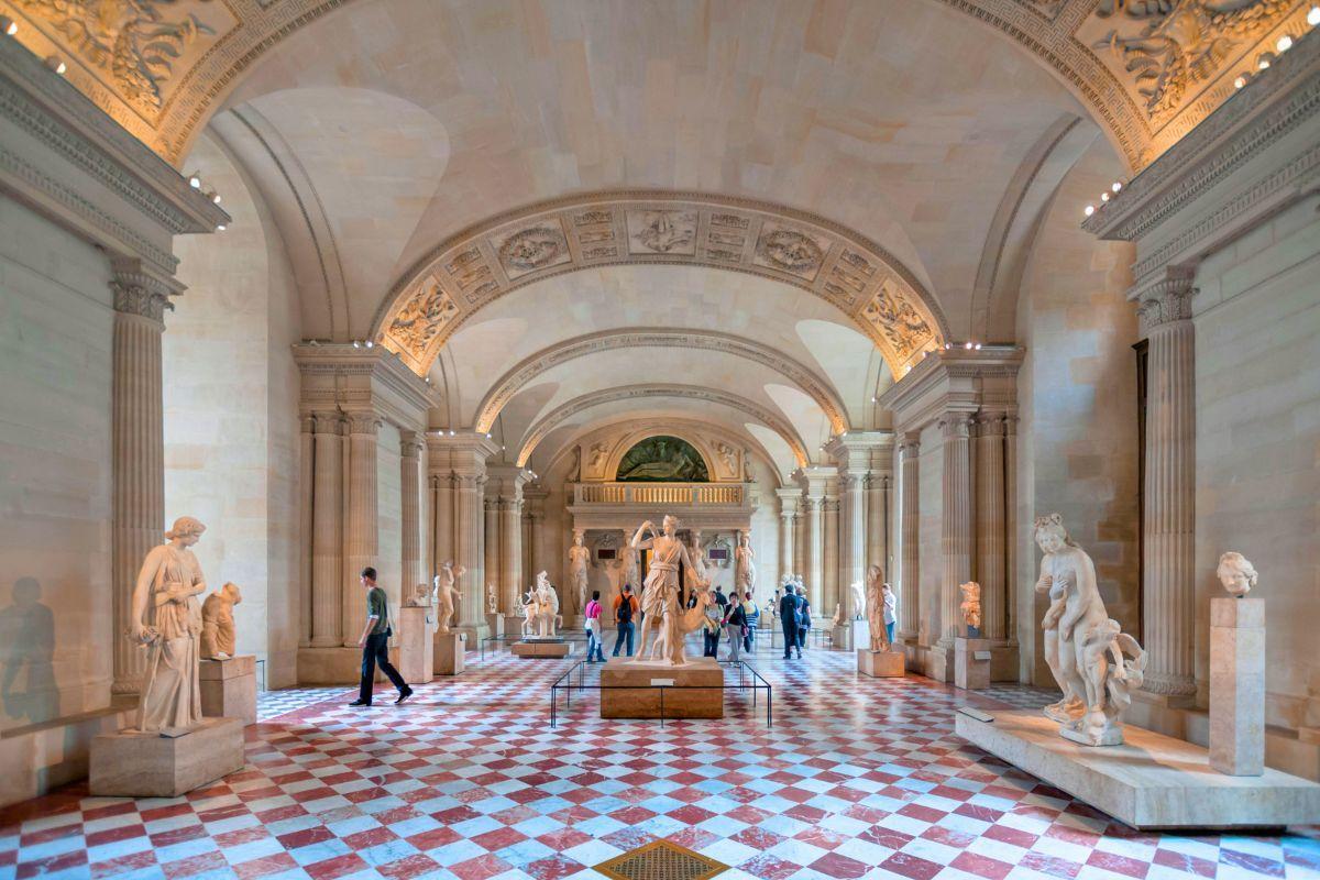 Visitors walking through a vaulted classical sculpture gallery with checkered marble floor