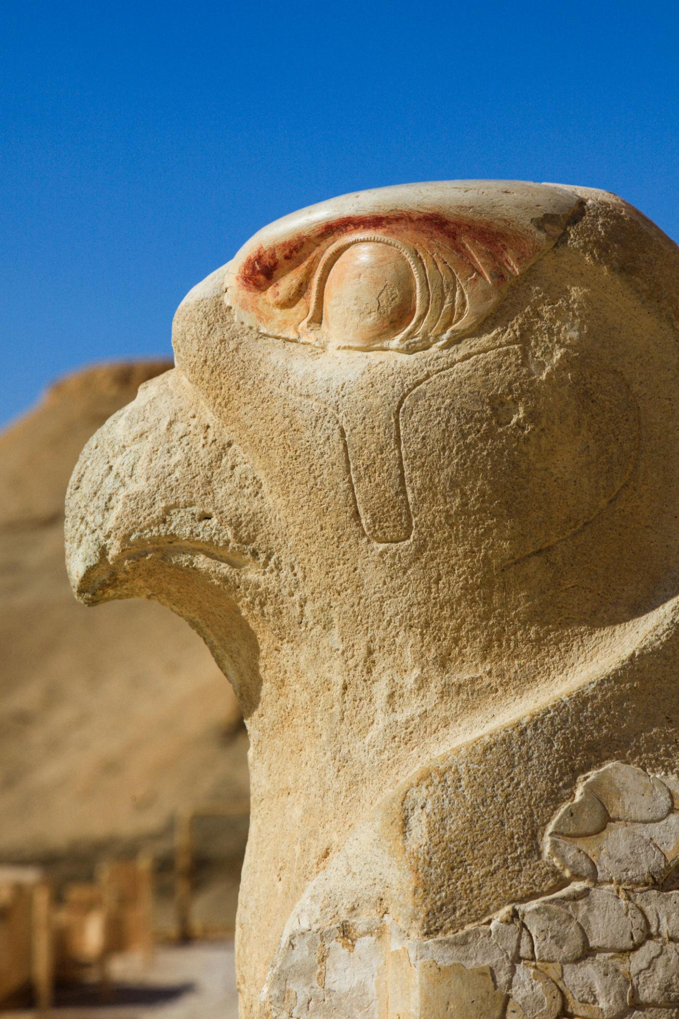 Close-up of carved Horus falcon head with painted eye against blue sky