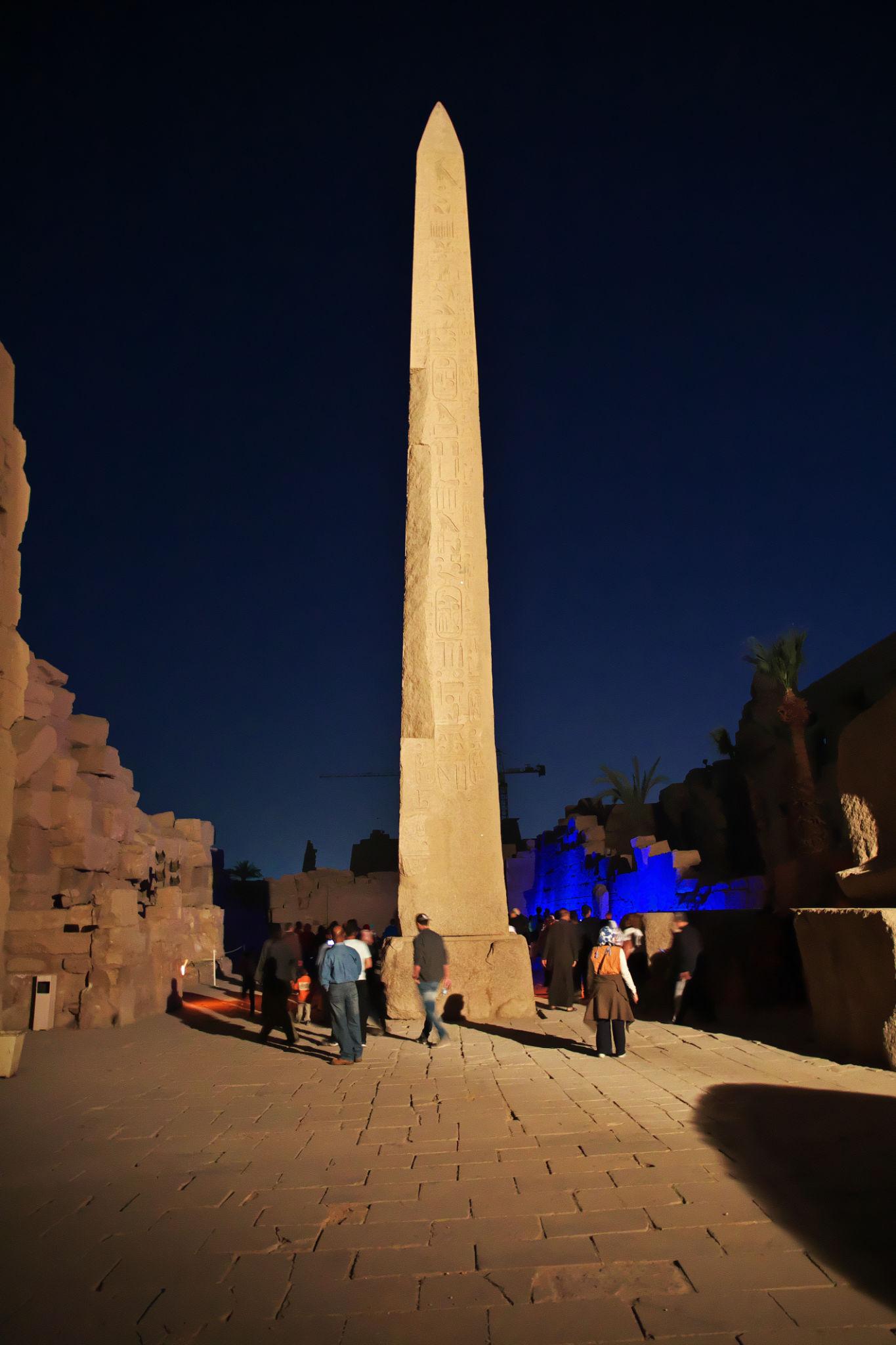 Visitors gather beneath Hatshepsut's obelisk lit against a deep night sky