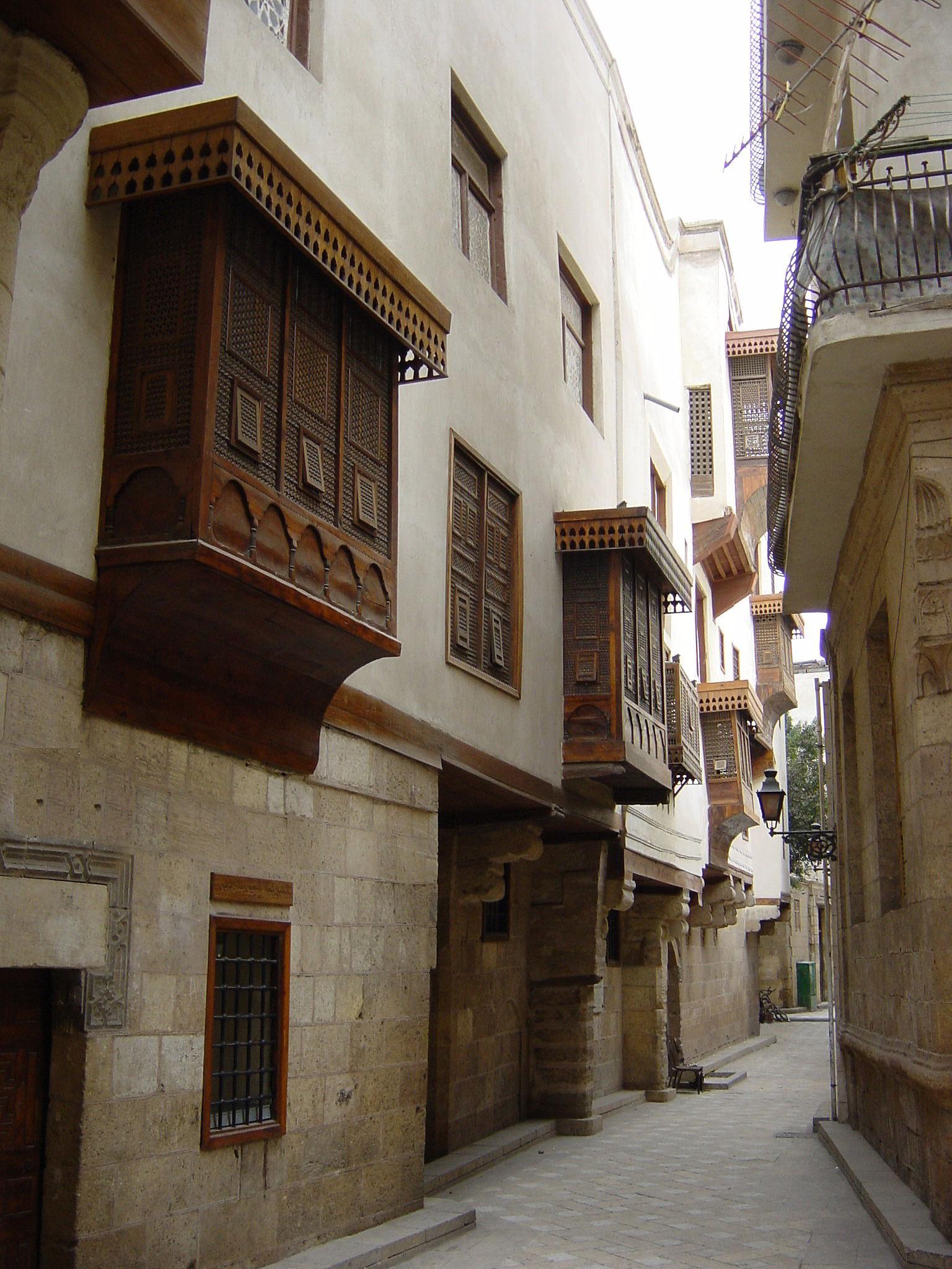 A narrow alley lined with ornate wooden mashrabiya bay windows on historic stone buildings