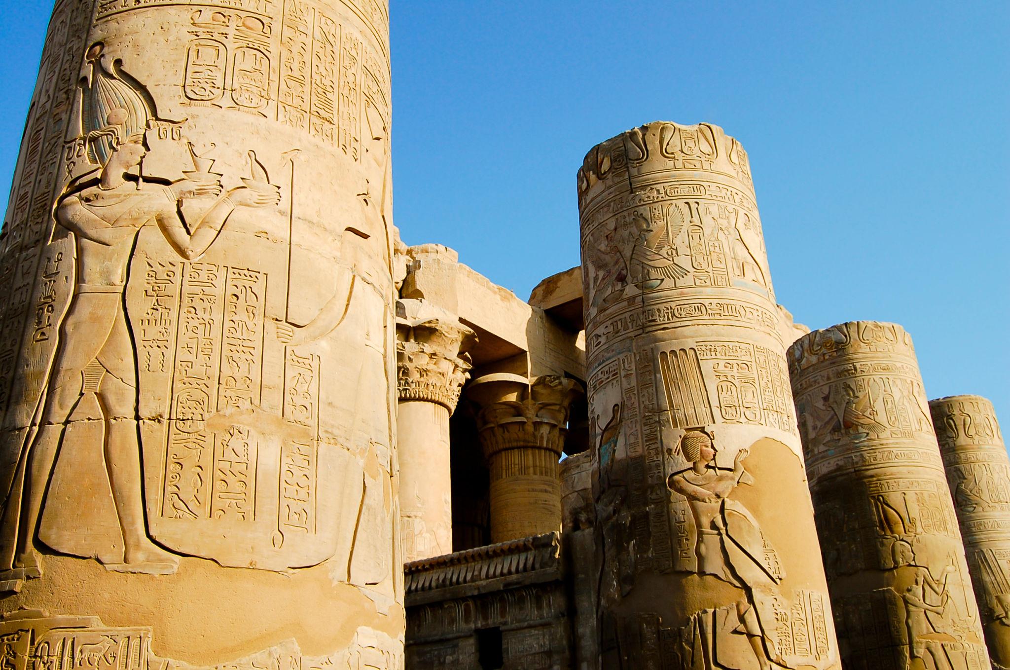 Towering carved columns with figures and hieroglyphs against a clear blue sky.