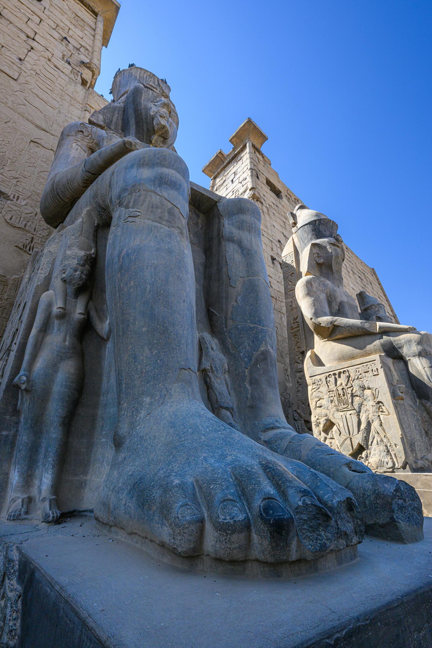Low-angle detail of a Ramses II colossus feet and legs at Luxor Temple.