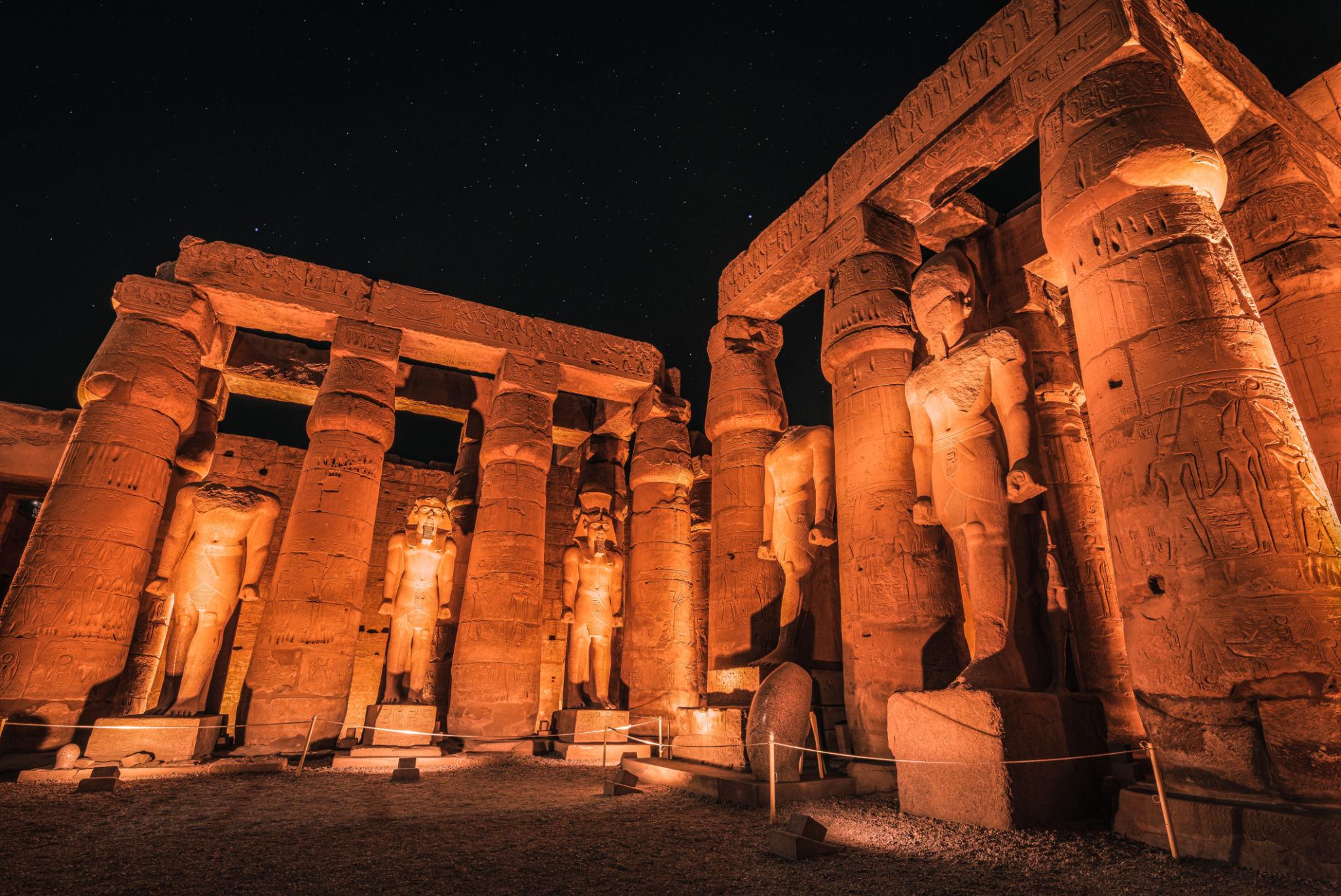Warmly uplit courtyard colonnade and statues of Luxor Temple at night.