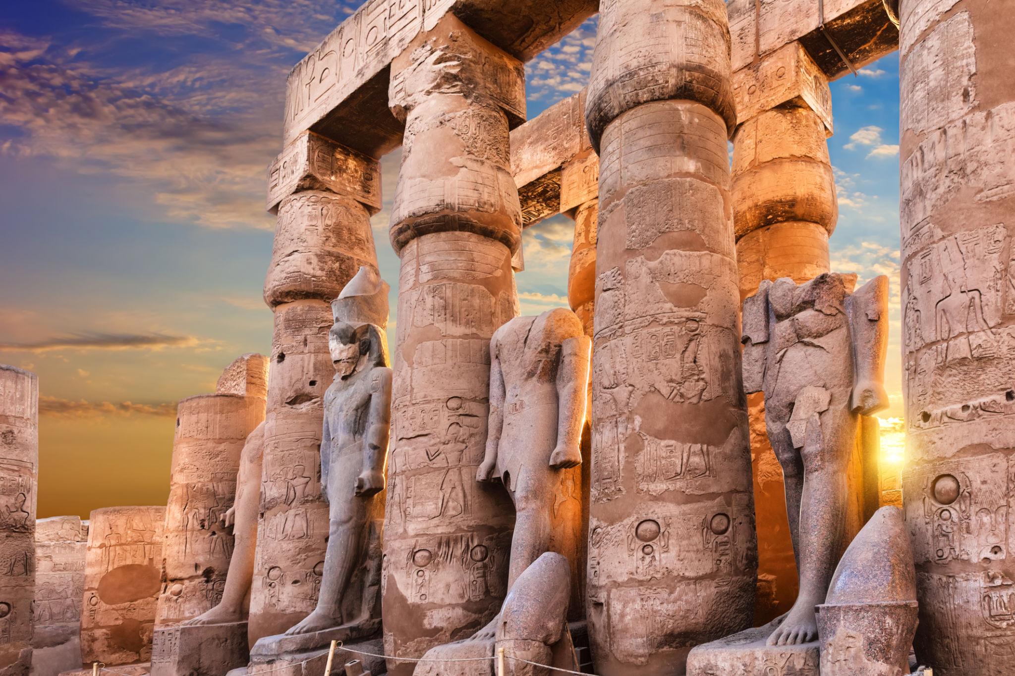 Ramses II statues between columns glowing in warm sunset light.