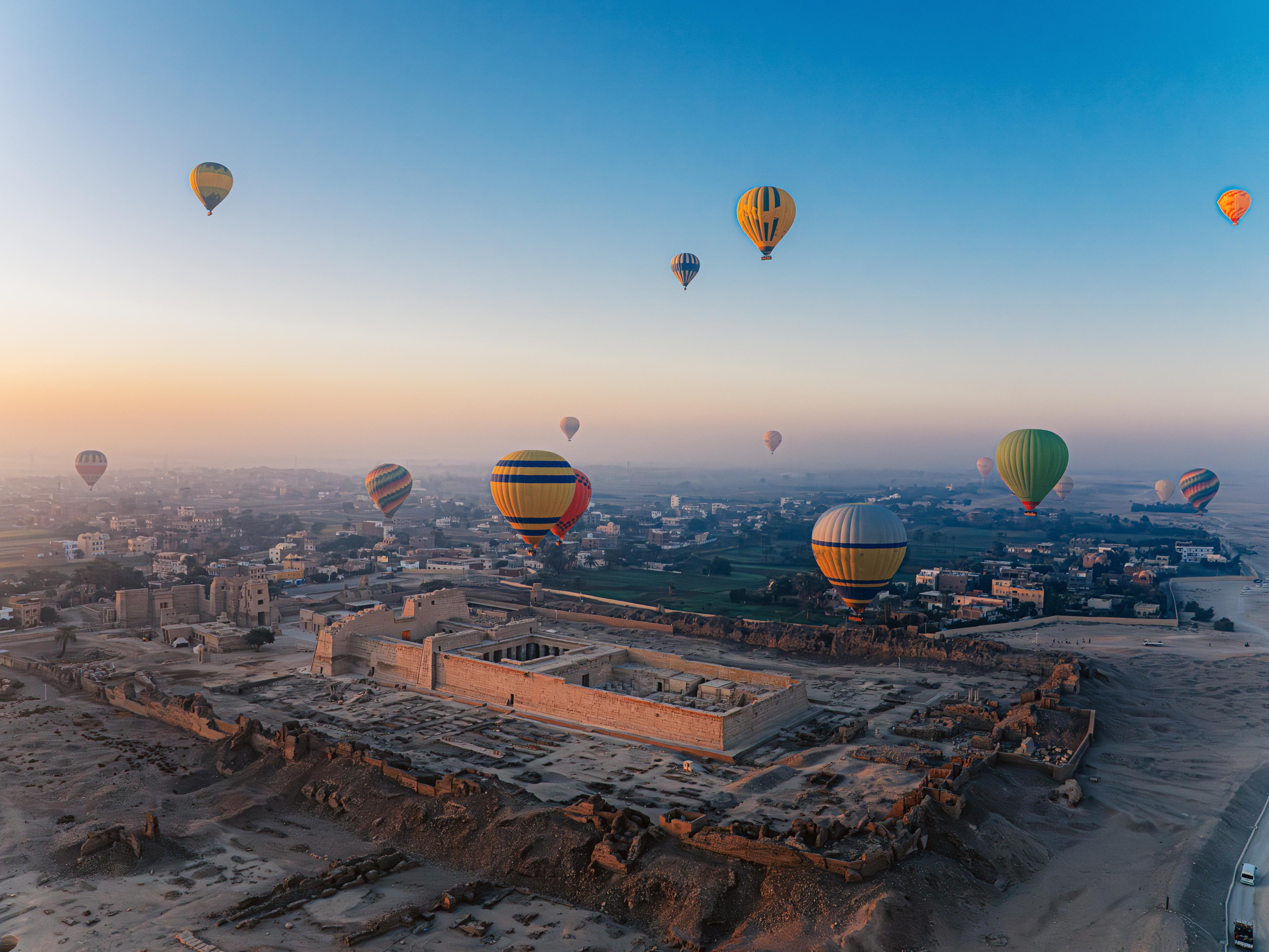 Hot air balloons drifting over Medinet Habu temple at sunrise on Luxor's west bank.