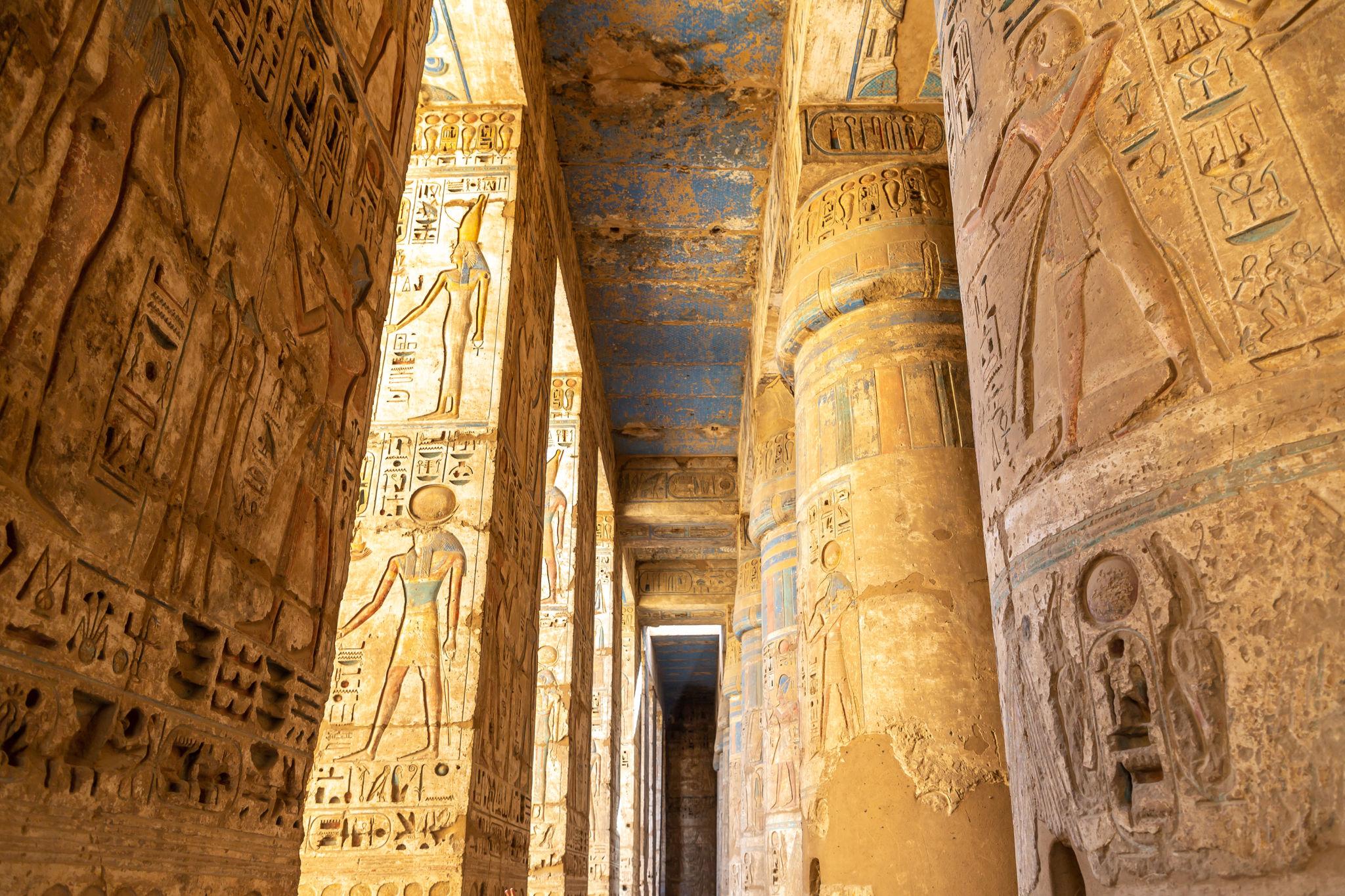 Sunlit Osiride pillars and painted reliefs in the second court of Medinet Habu.