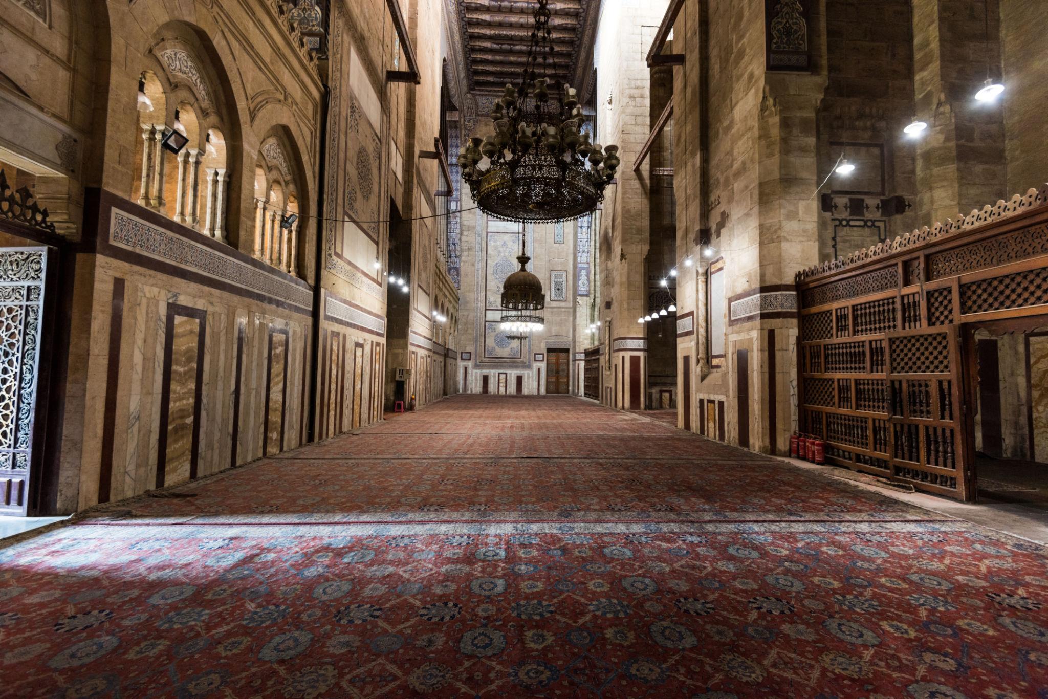 Vast carpeted prayer hall with hanging chandelier and towering vaulted iwan walls