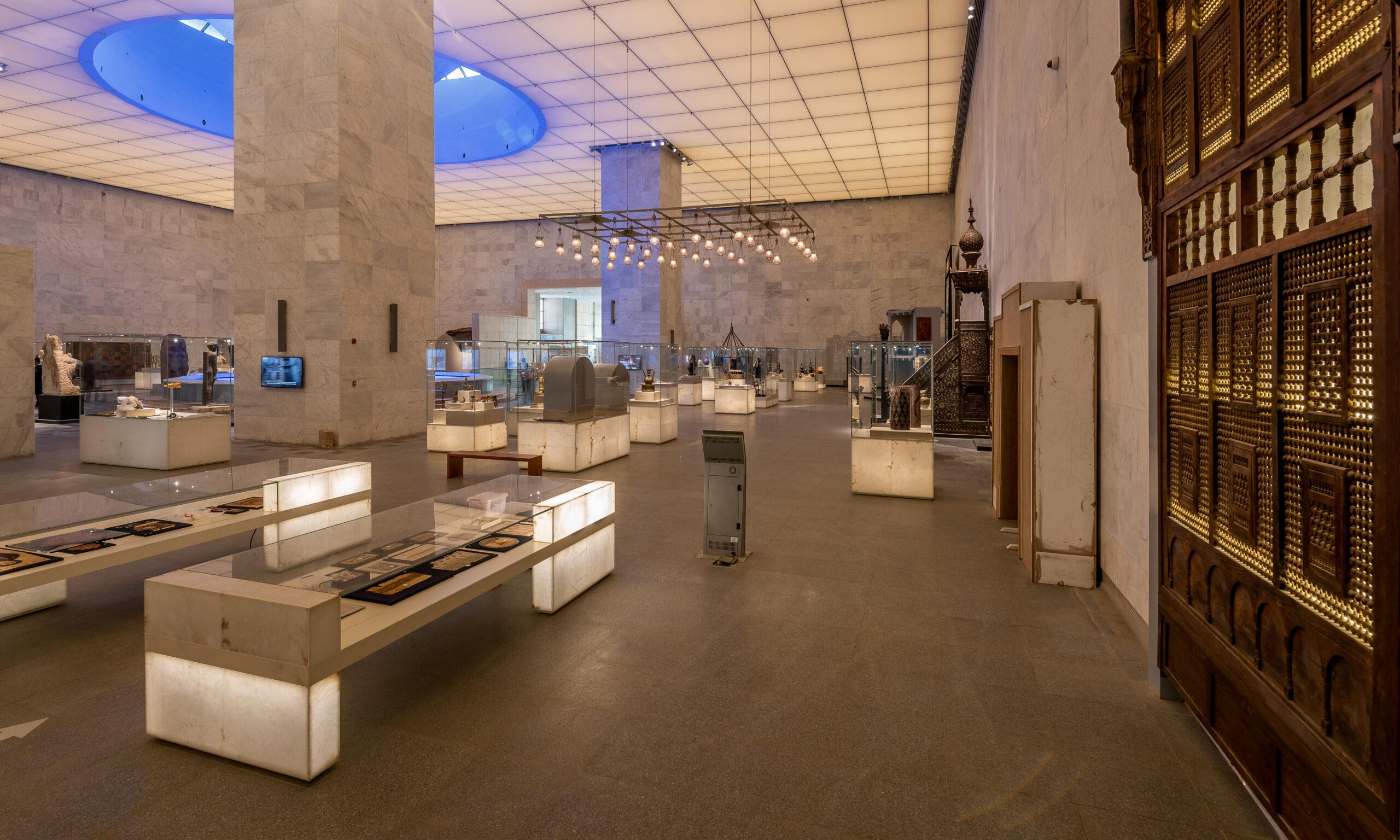 Spacious NMEC gallery with illuminated display cases and ornate wooden Islamic door panel