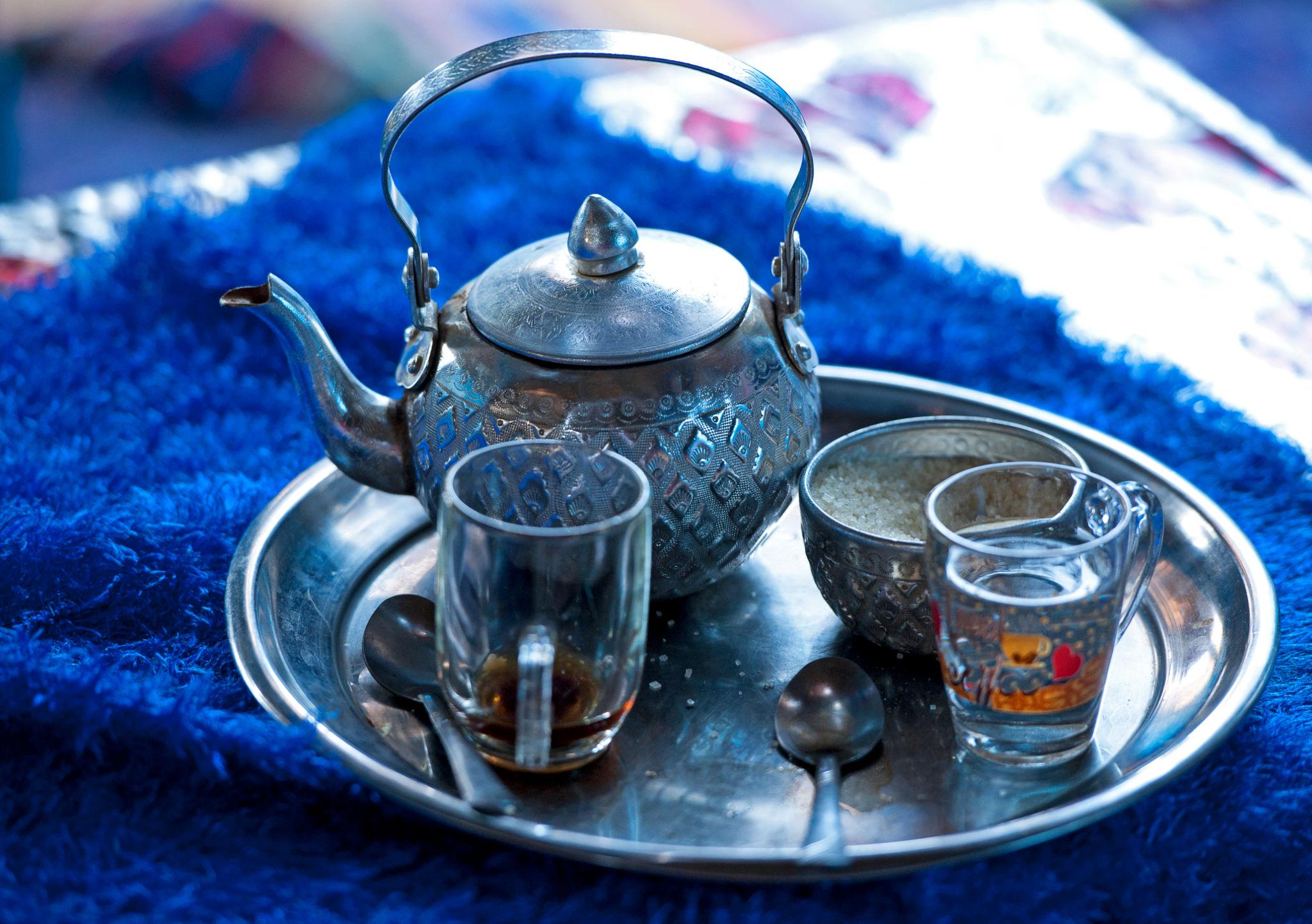 An ornate silver teapot with two glass cups and sugar bowl on a metal tray