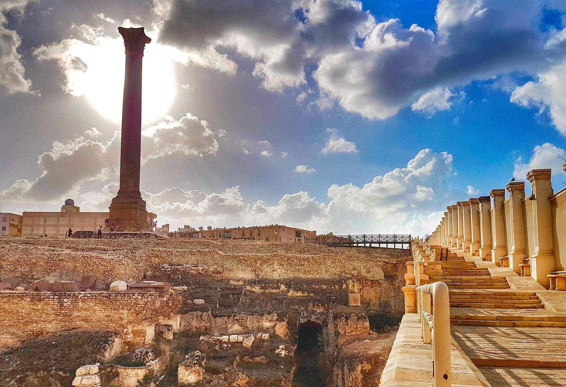 Pompey's Pillar and Serapeum ruins with staircase under a dramatic cloudy sky