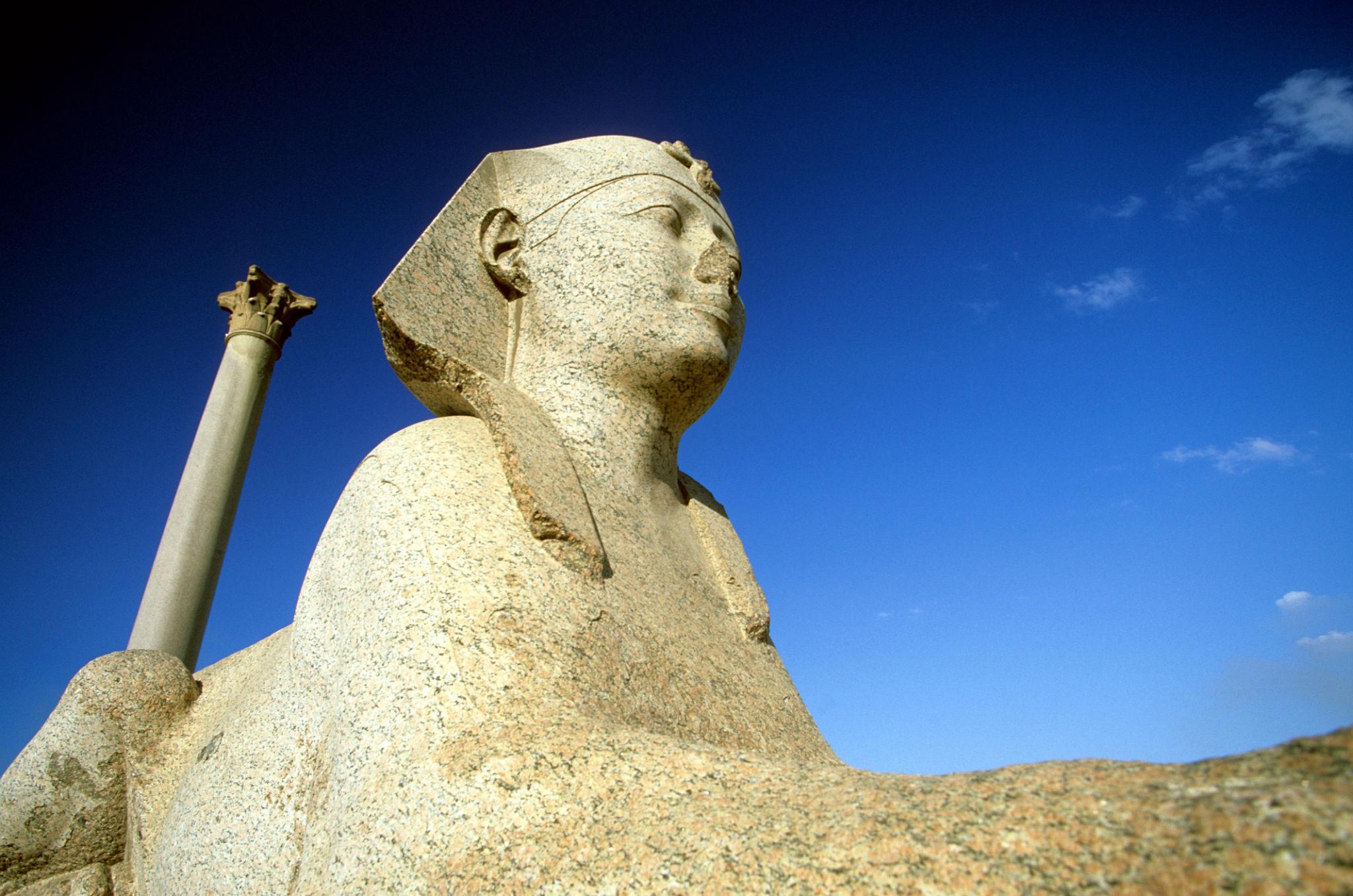 Granite sphinx head in foreground with Pompey's Pillar rising against a deep blue sky