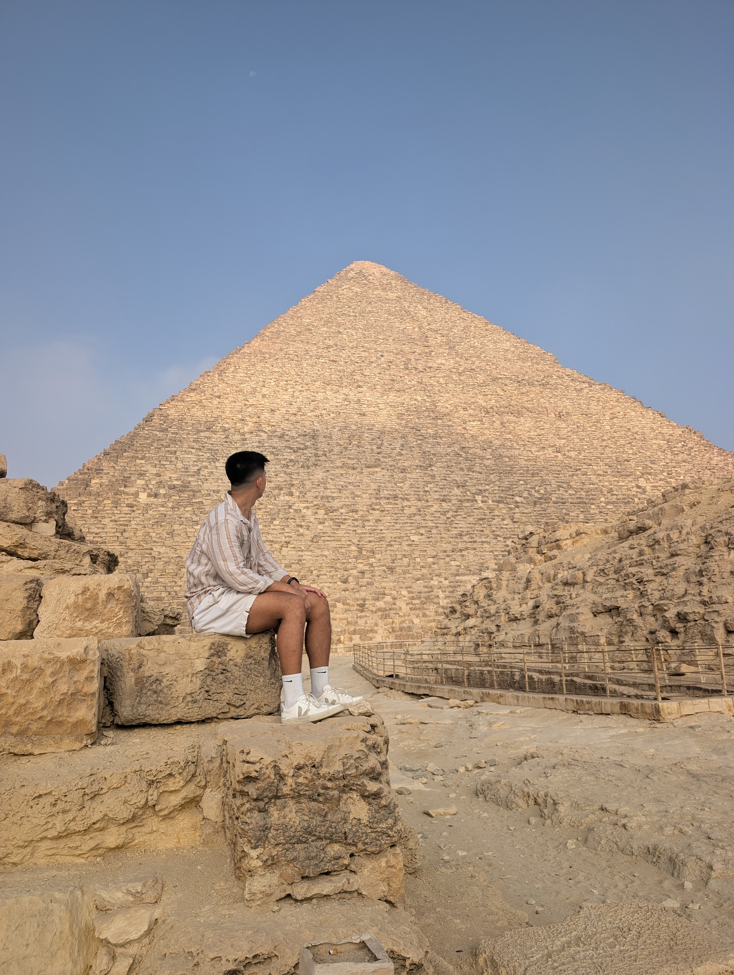 Young visitor seated on stone blocks gazing up at the Great Pyramid of Khufu