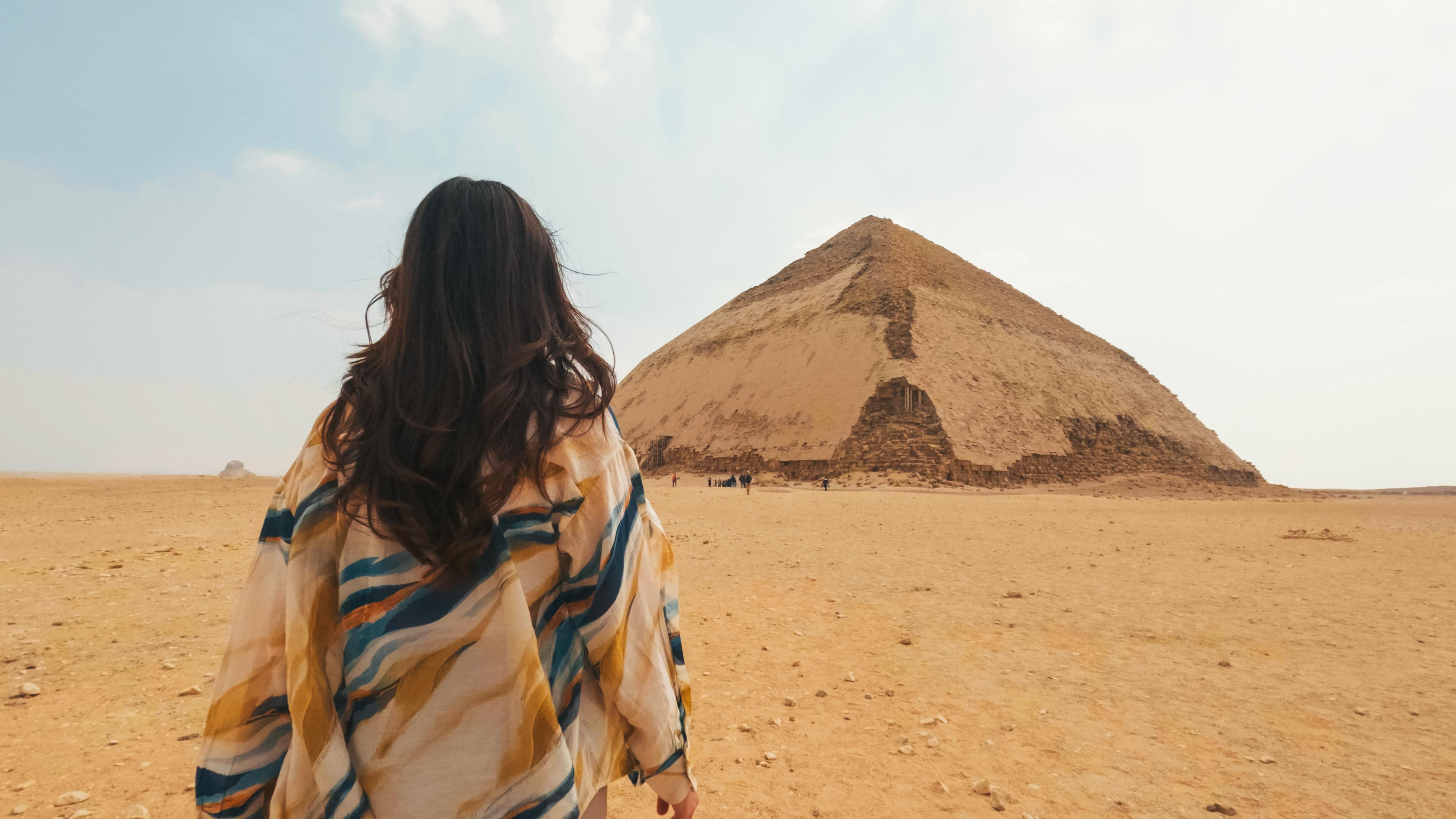 A woman in a colorful wrap gazes toward the Bent Pyramid rising from the desert at Dahshur.