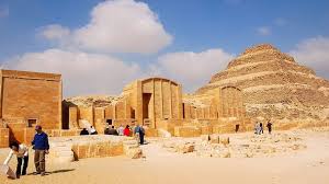 Tourists exploring the ancient stone courtyard with the Step Pyramid of Saqqara in the background