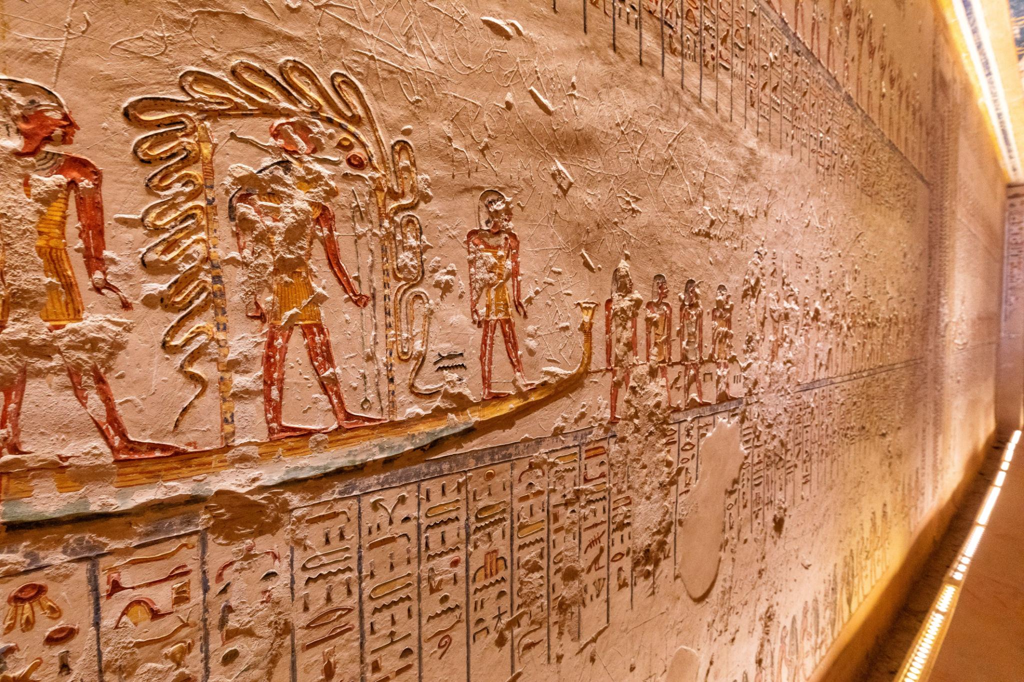 Close-up of sunken relief figures and hieroglyphs carved into a Valley of the Kings tomb wall.